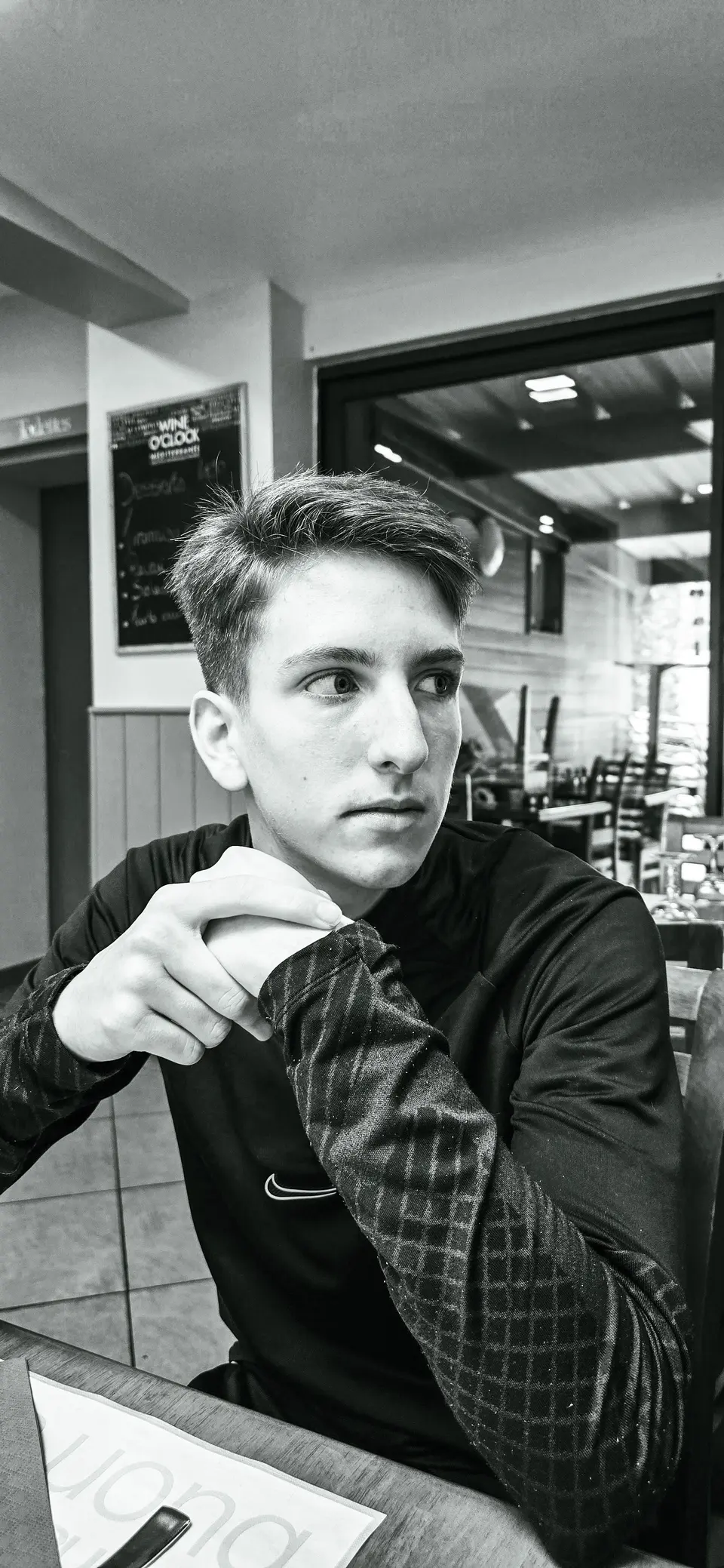 Portrait en noir et blanc d'un jeune homme pensif, accoudé à une table